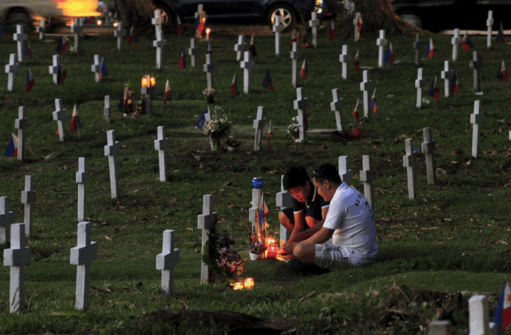 Father and son light candles in a cemetery during Undas